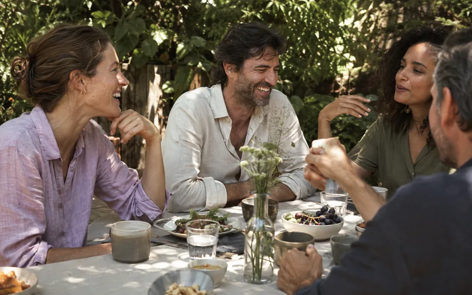Friends gathered around a garden table in afternoon light. An illustrative community scene.