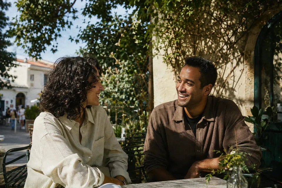 Two adults sharing a laugh at a sunlit garden café. An illustrative brand scene.